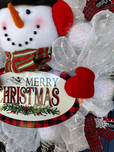 Close Up Detail of Black and Red Buffalo Plaid Bordered Oval Sign with the words Merry Christmas with garland that the Snowman holds wearing Red Mittens.