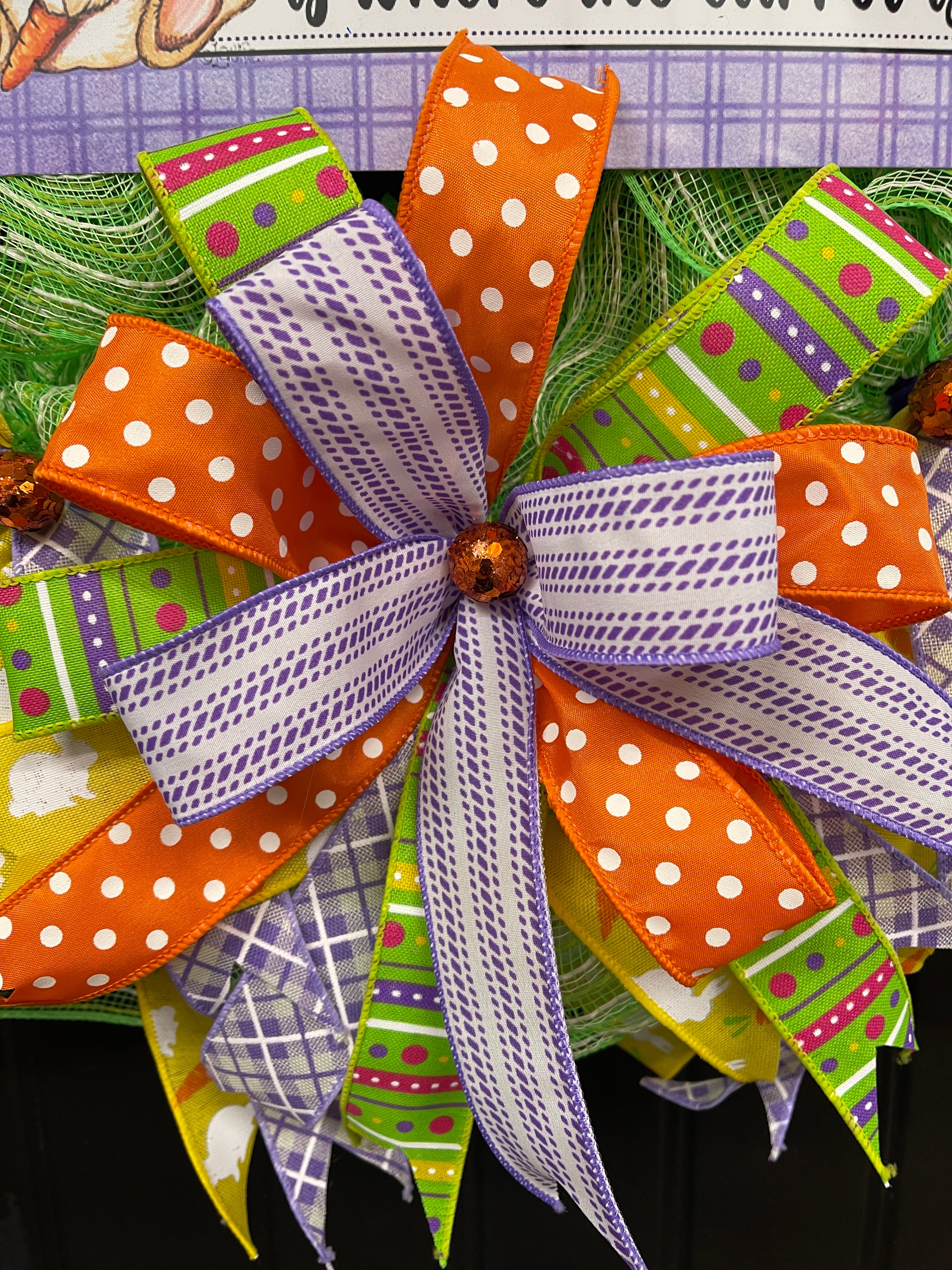 Close Up of Bow with Purple, White, Orange, Pink, and Green Ribbons with an Orange Ball in the Center