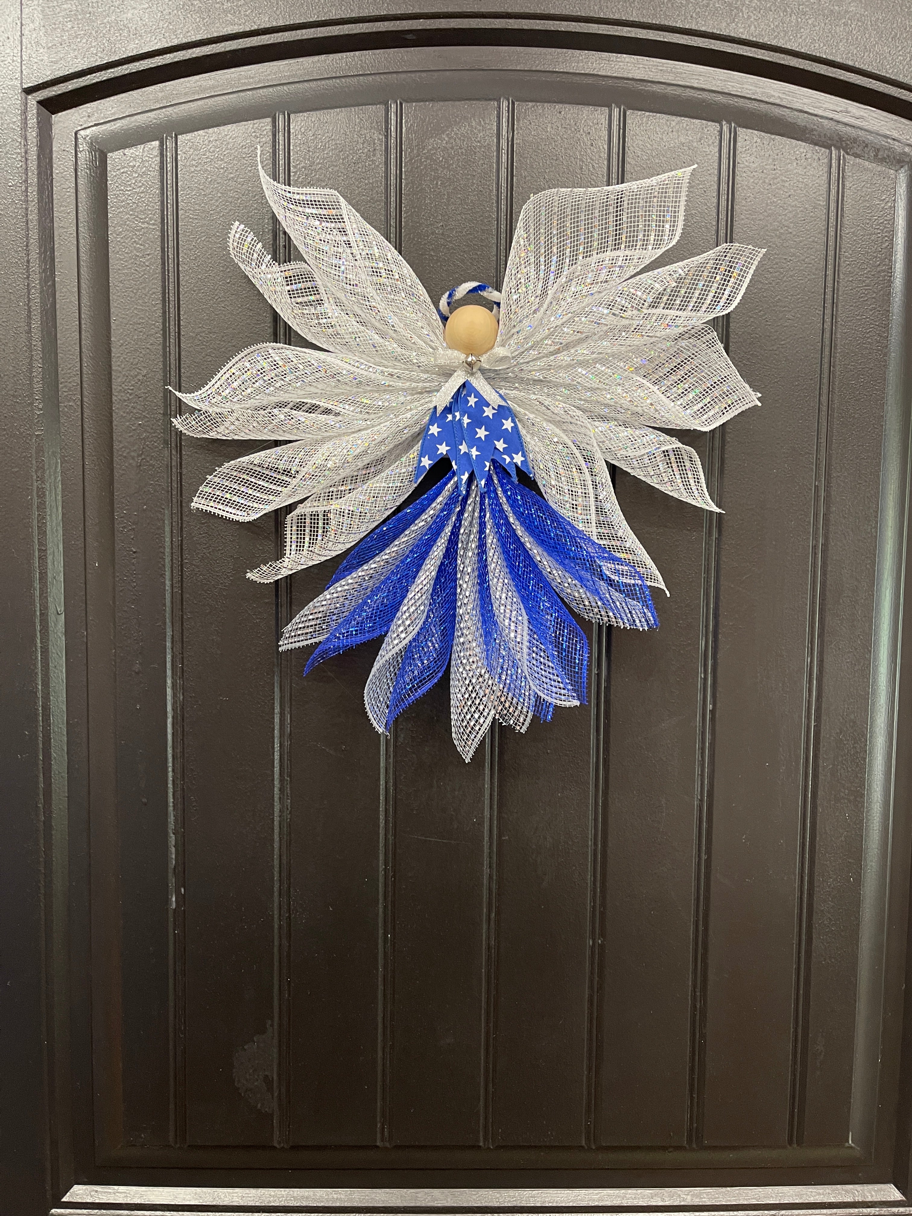 Blue, white and silver deco mesh angel with blue ribbon with white stars, wooden head, silver bow and bell with blue and white halo on a black door. 