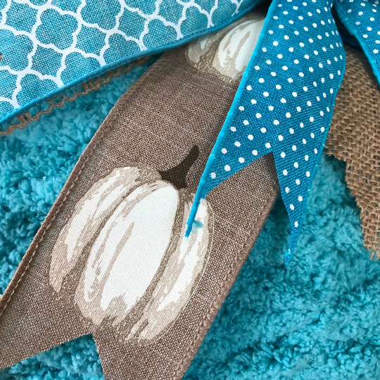 Close Up of Ribbon from Bow featuring white pumpkins on a tan ribbon. 