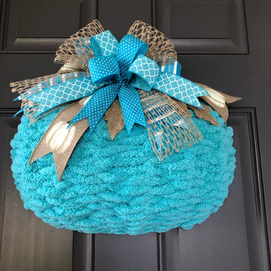 Upward View of Blue Chenille Yarn Pumpkin Wreath with Blue, White and Beige Bow at the top on a Gray Door. 