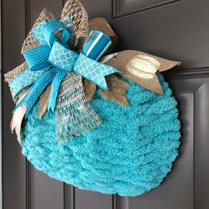 Right Side View of Blue Chenille Yarn Pumpkin Wreath with Blue, White and Beige Bow at the top on a Gray Door. 