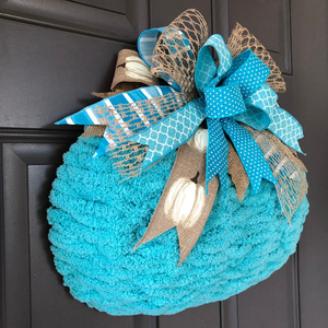 Left Side View of Blue Chenille Yarn Pumpkin Wreath with Blue, White and Beige Bow at the top on a Gray Door. 