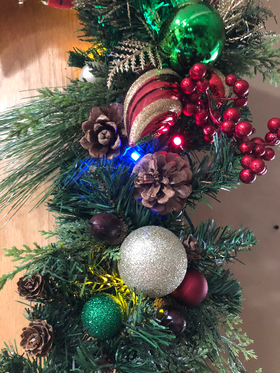 closeup of the pine cones, red berries, and glitter Christmas balls on the Christmas lighted garland or corner swag