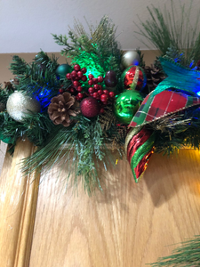 closeup of the evergreen swag with red berries, multi-colored Christmas ornaments, and multi-colored lights on the lighted garland home decor