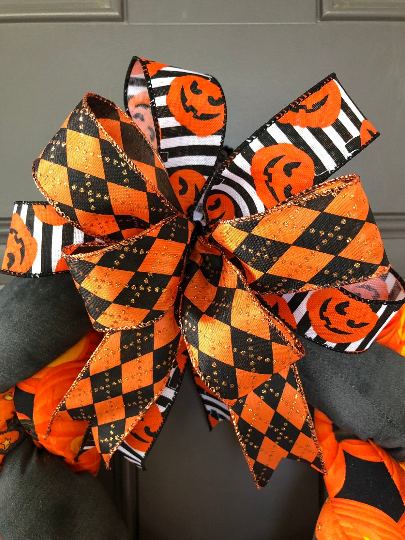 Close Up of Bow Featuring Black and Orange Harlequin Print, Smiling Pumpkins on a Black and White Striped Ribbon 