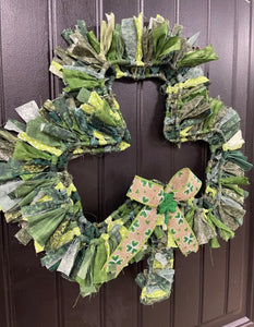 Left Side View of Various Light and Dark Shades of Green Cotton Fabric tied onto a Clover Shaped Frame topped off with a beige and clover ribbon and a glittered green shamrock on a black door. 
