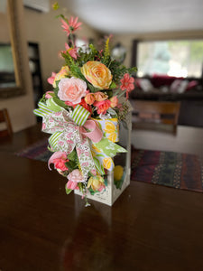 Pastel Green, Yellow, Peach and Pink Ranunculus, Tulips, Poppies and Roses along with Meadow Flowers  with a Bow Swag on a White Lantern
