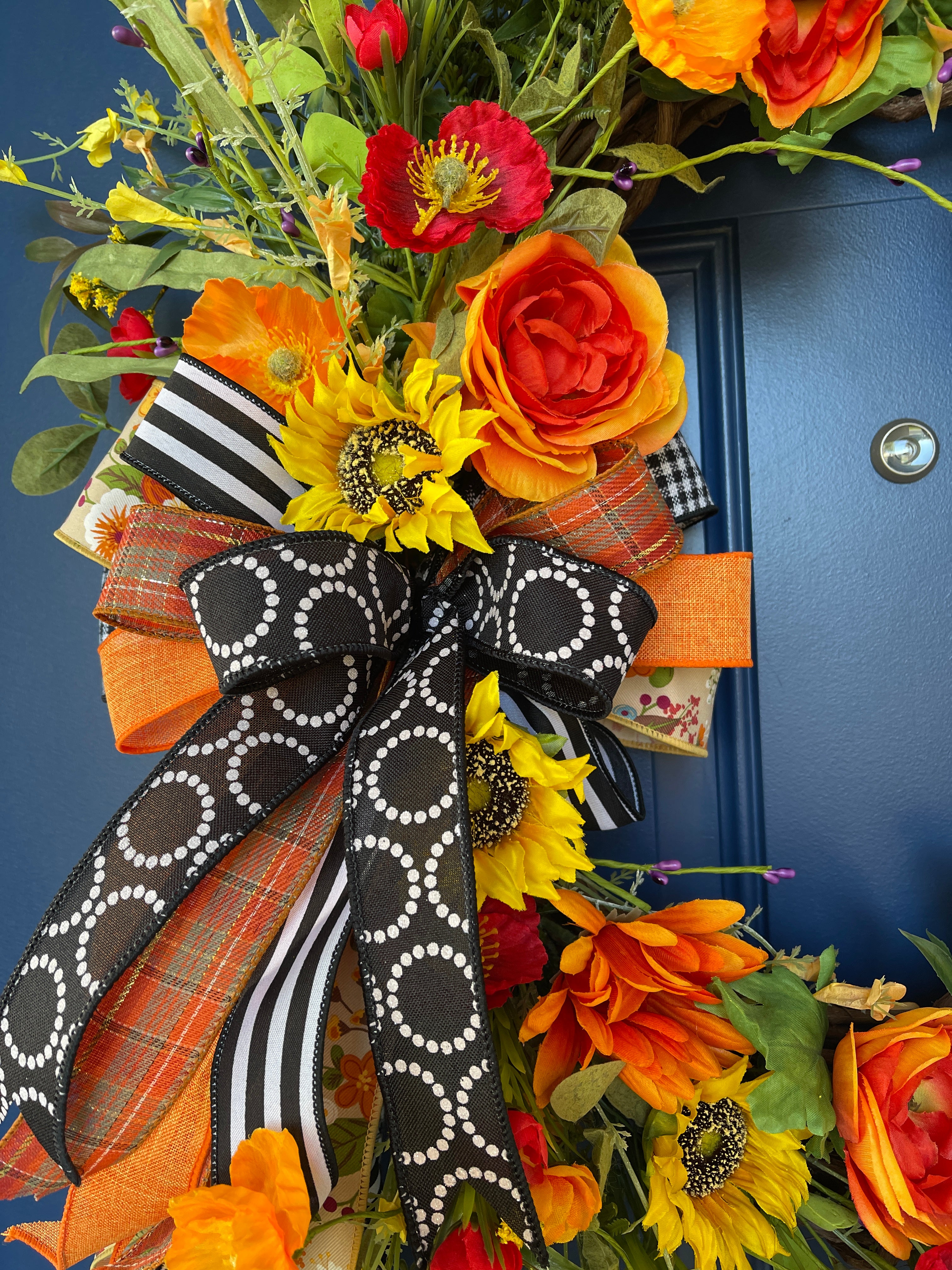Close Up Detail of Bow Featuring Black and White Polka Dot Circles Ribbon, Fall Orange, Green and Gold Plaid Ribbon, Solid Orange Ribbon, Black and White Gingham Ribbon, Black and White Striped Ribbon along with Orange and Red Poppies, Sunflowers and Ranunculus 