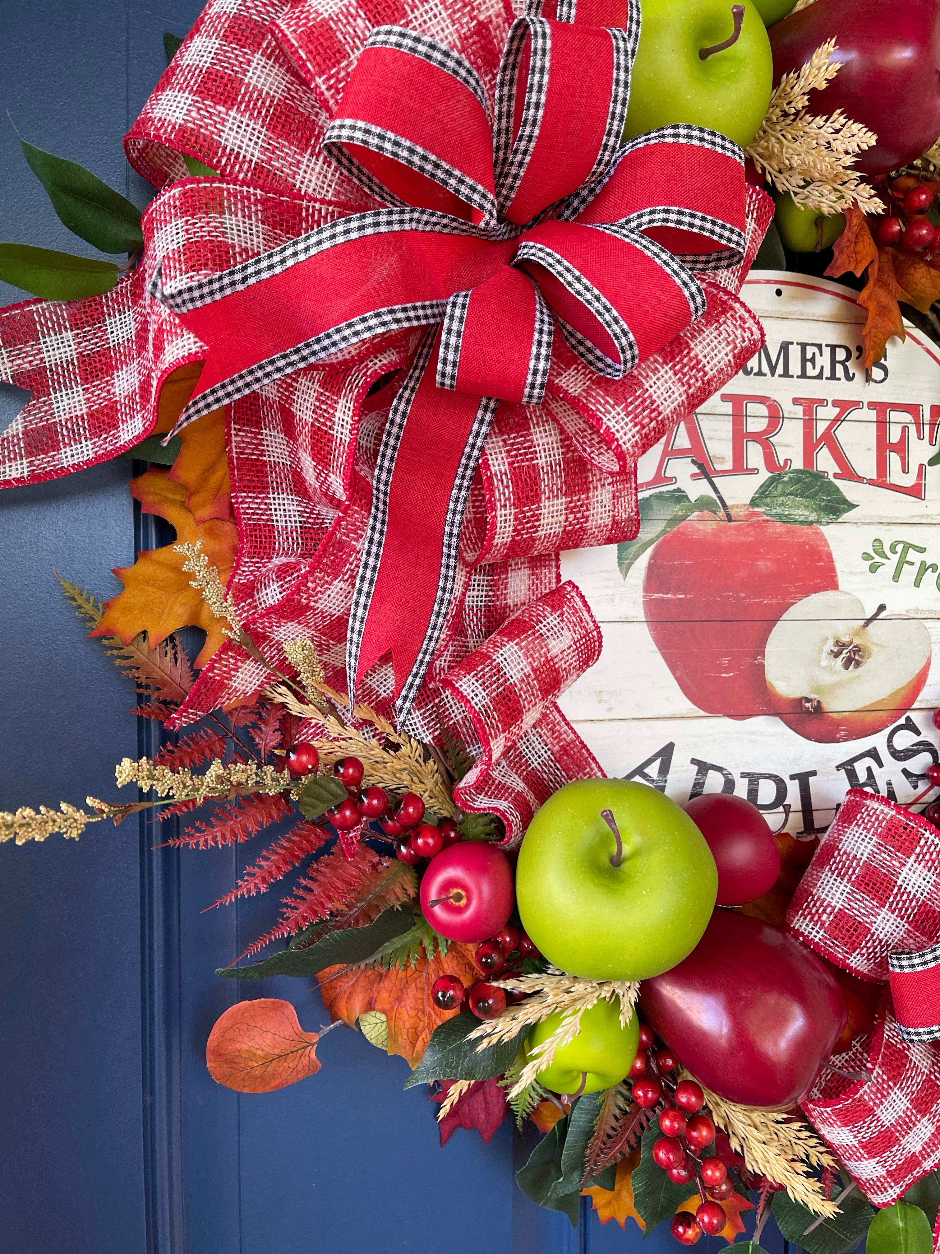 Left Side Lower View of Fall Apple Grapevine Wreath filled with Red and Green Apples, Fall Leaves and Berries, Double Bows of Red, White and Black with a Farmers Market Fresh Apples Sign in the Center. 