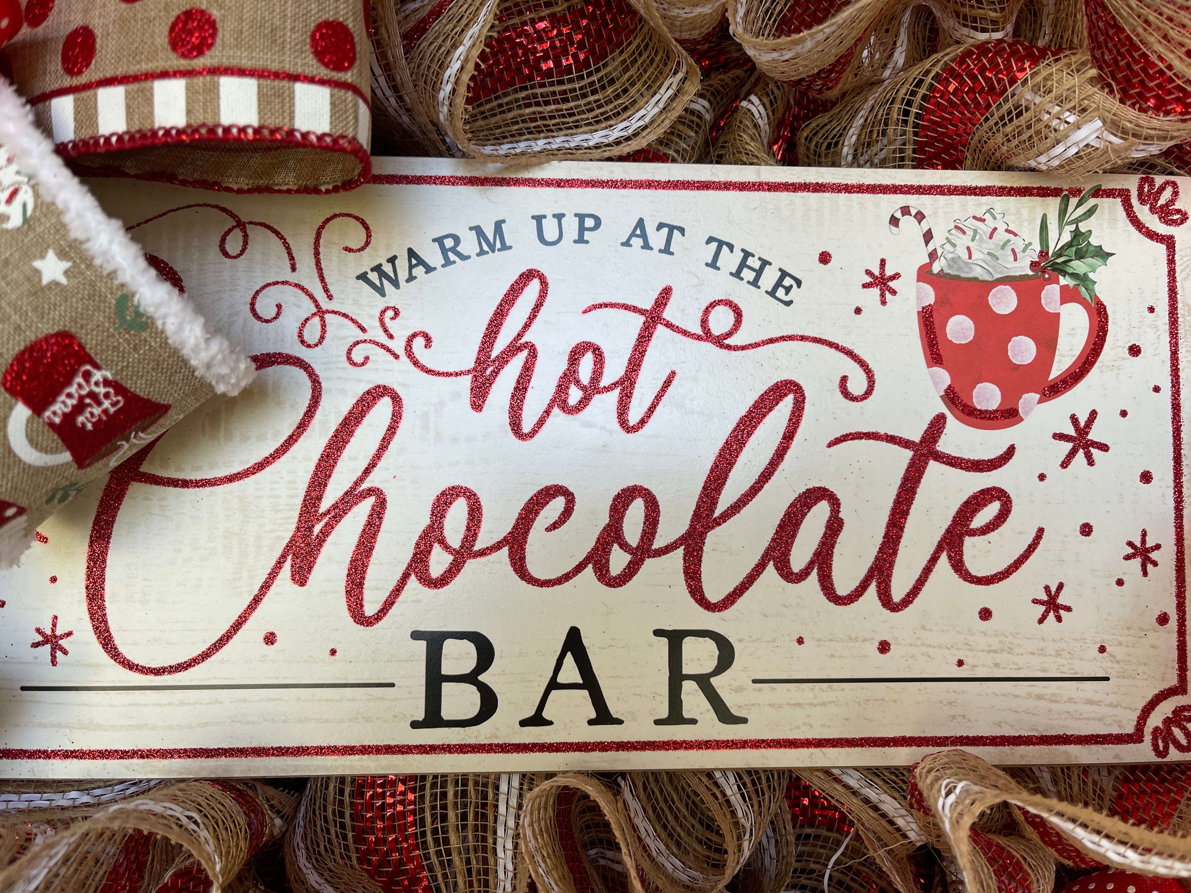 Close Up of Warm Up at the Hot Chocolate Bar Sign with a cup of cocoa with whipped cream and a candy cane. 