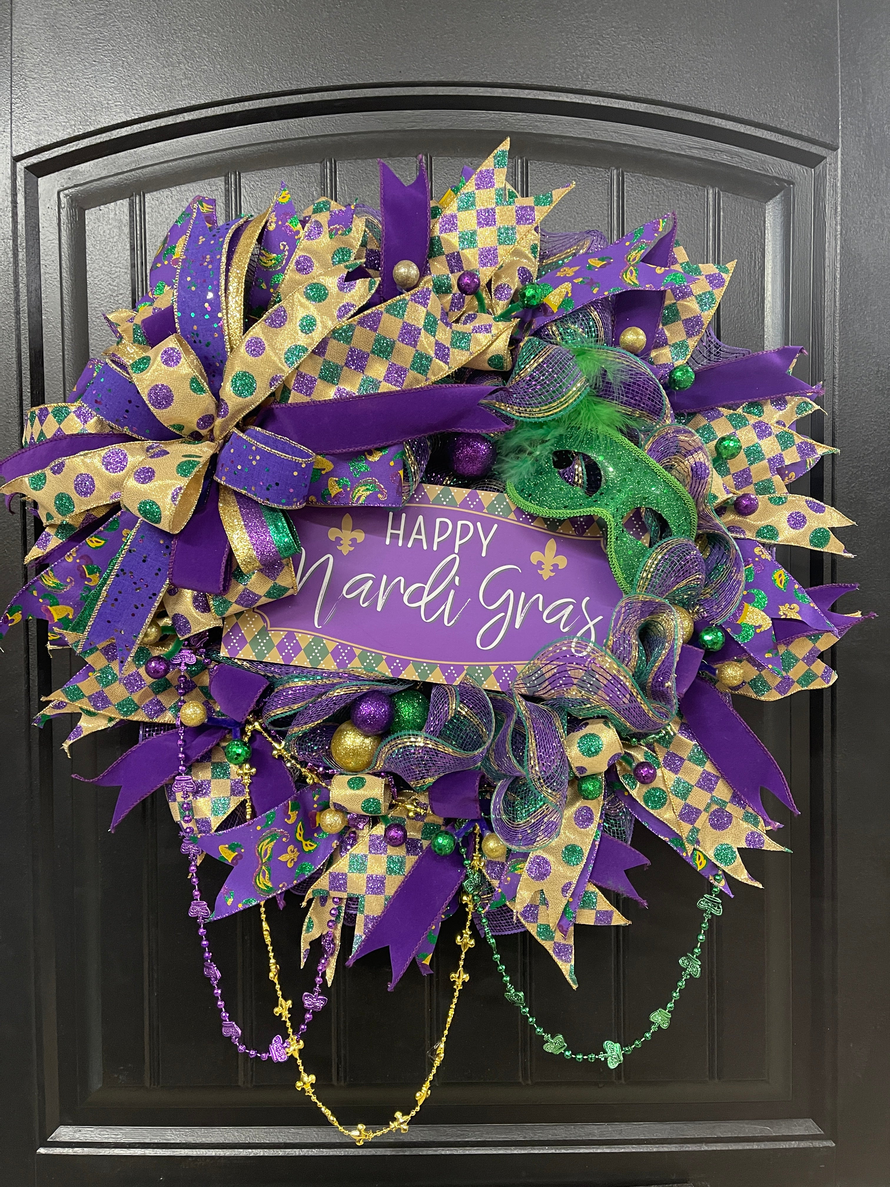 Purple, Green and Gold Mardi Gras Wreath with Beads, Balls, Mask and Bow on a Black Door