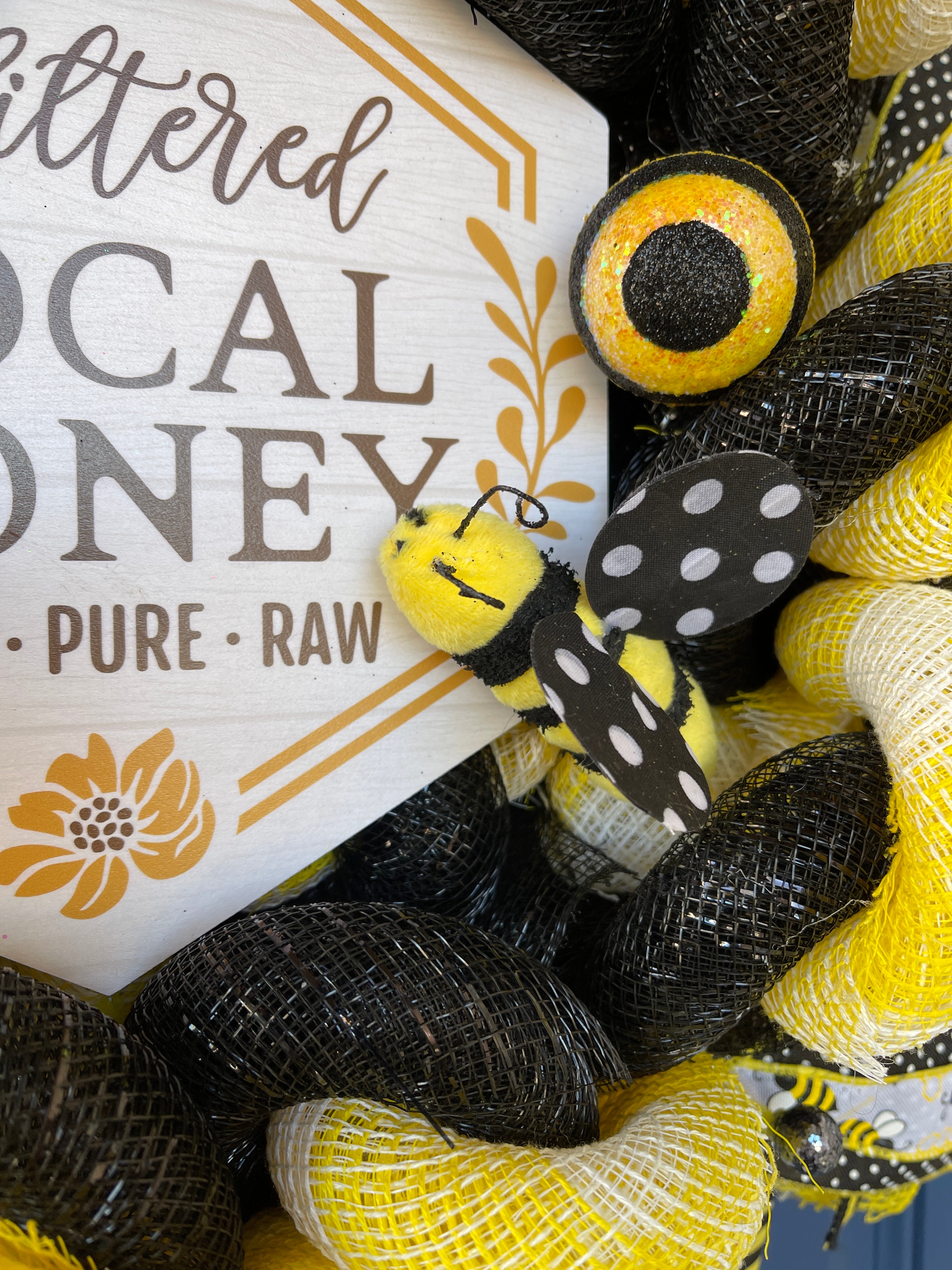 Close of up Fuzzy Bumble Bee with Black and White Polka Dot Wings next to sign on Bumble Bee Local Honey Black and White Wreath for Front Door