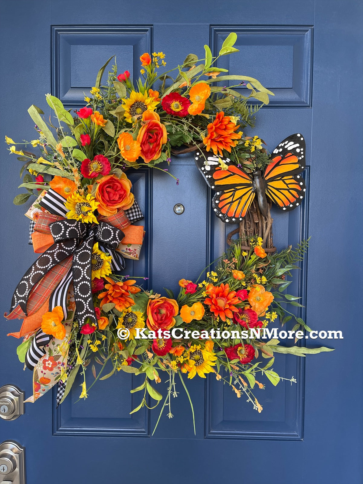 Orange and Yellow Monarch Butterfly Sunflower and Ranunculus Floral Grapevine Wreath with a Bow on a blue door. 
