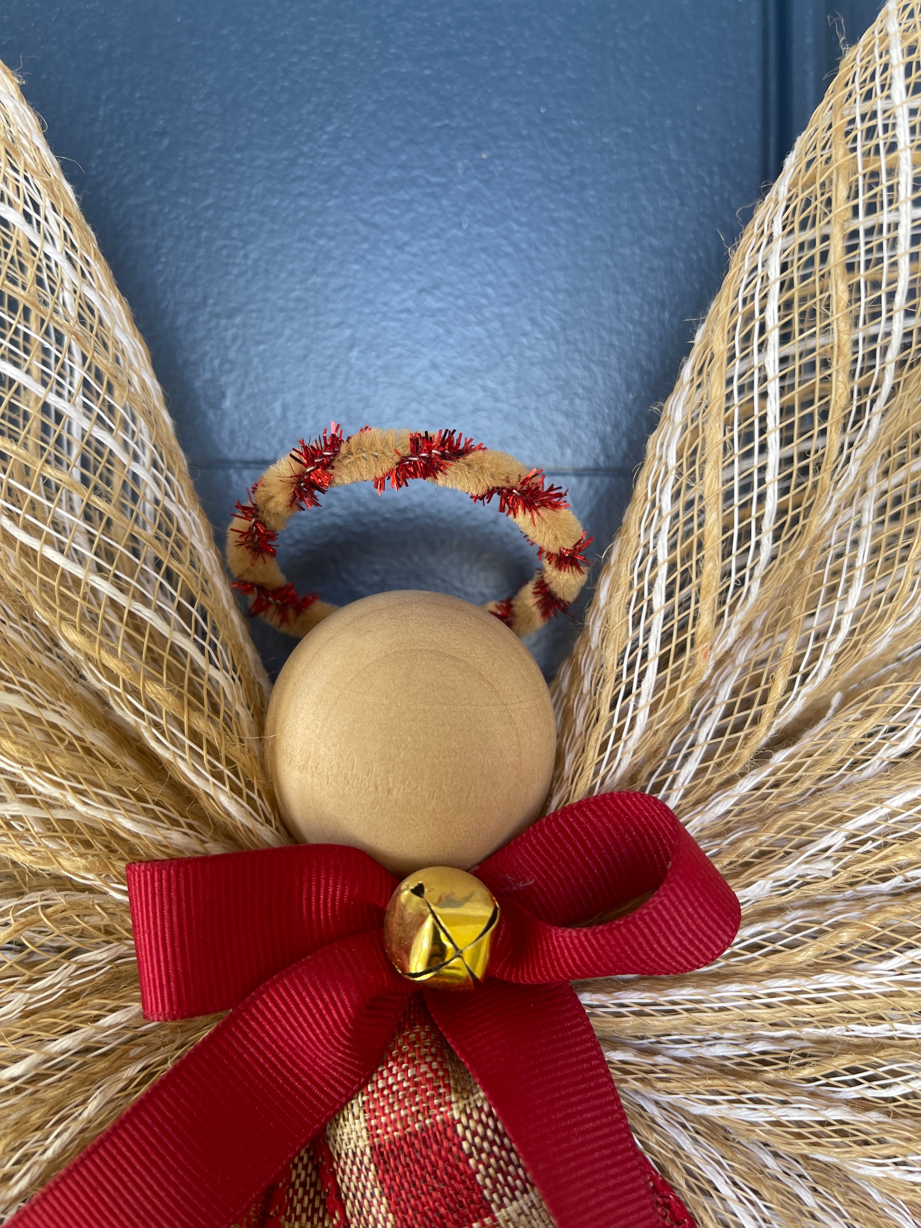 Close Up View of Wooden Head, with a Tan and Red Metallic Halo, Gold Bell on a Red Bow and Red and Tan Plaid Apron