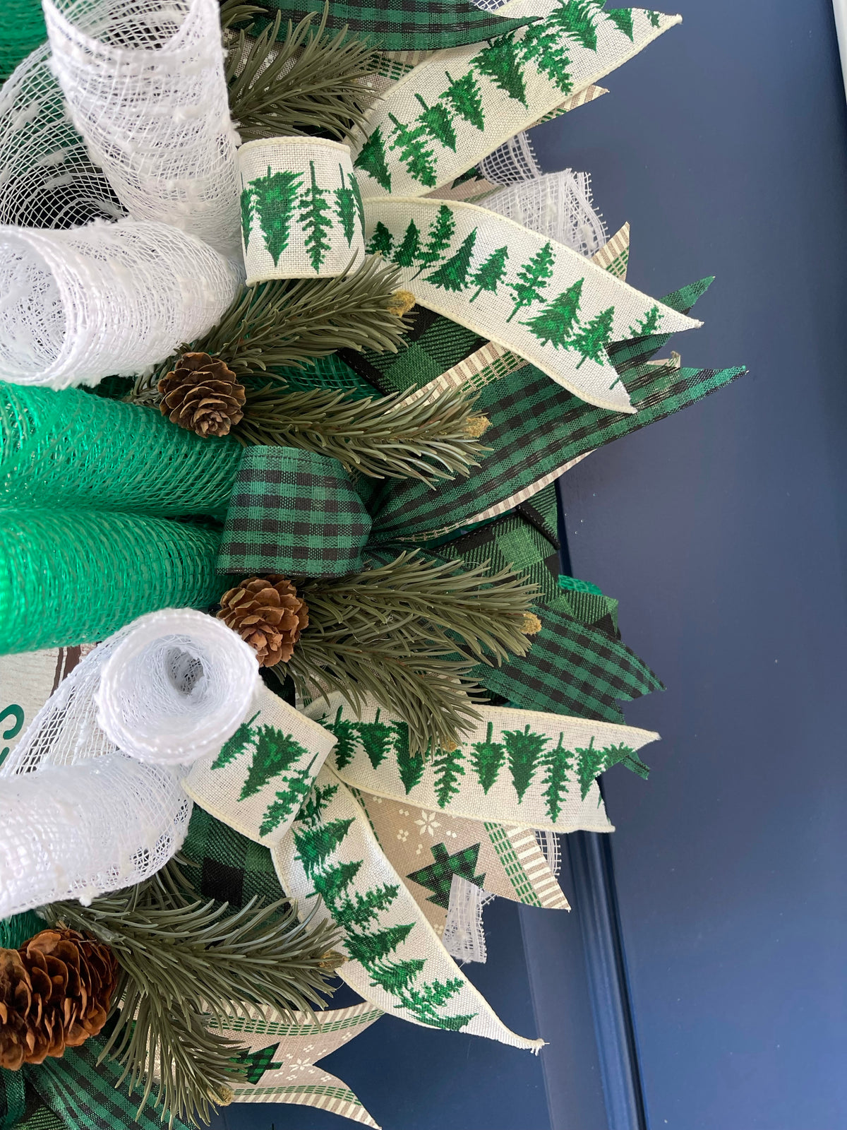 Close Up of Artificial Pine Sprigs with Pine Cones among Black, White and Green Ribbons on A Deco Mesh Wreath