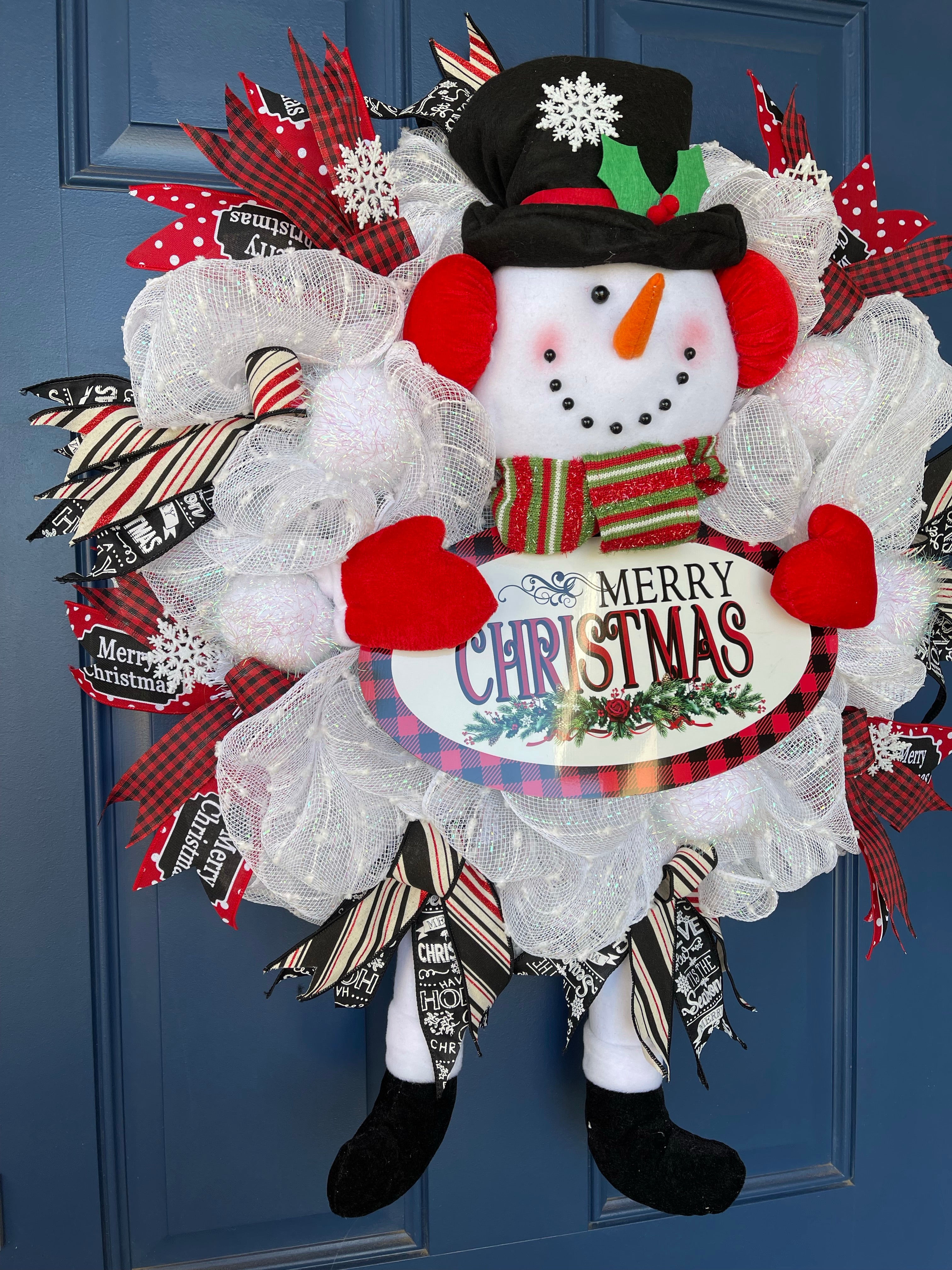 Left Side View of Red, White and Black Snowman Plush Deco Mesh Wreath holding a Merry Christmas Sign on a blue door