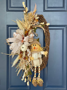 Plush Scarecrow with Shovel on a Grapevine wreath with White, Tan, and Light Brown Florals and Berries on a Blue Door