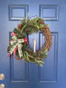 Christmas Grapevine Wreath with Artificial Pine Branches, Red Berries, Pinecones, with a Red, White and Green Bow and an Artificial Battery Operated Candle in the Center on a Blue Door