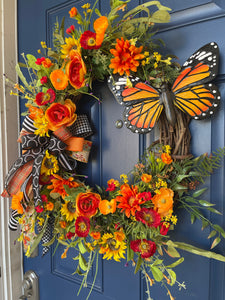 Right Side View of Orange and Yellow Monarch Butterfly Sunflower and Ranunculus Floral Grapevine Wreath with a Bow on a blue door. 