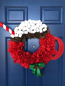 Red Burlap Wreath in the Shape of a Cup of Hot Cocoa with White Foam Marshmallows, a peppermint stick straw and a red wood handle on the cup with a green bow on a blue door. 