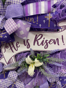 Close Up pf He Is Risen White and Purple Banner Sign with White Lilies and Sprigs of Artificial Lavender on a Lavender Deco Mesh Wreath