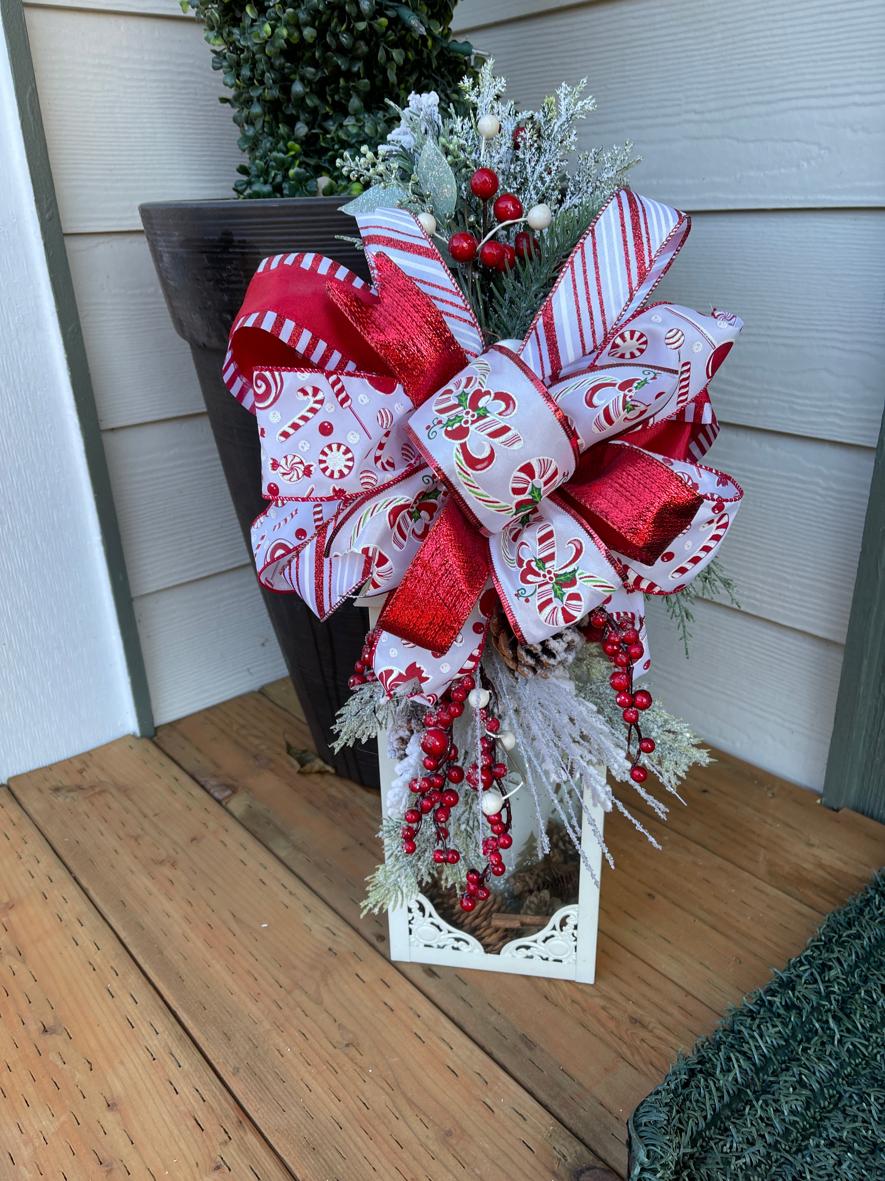 Red and White Candy Cane and Peppermint Lantern Swag with Evergreen Florals and Red Berries on a wood porch. 