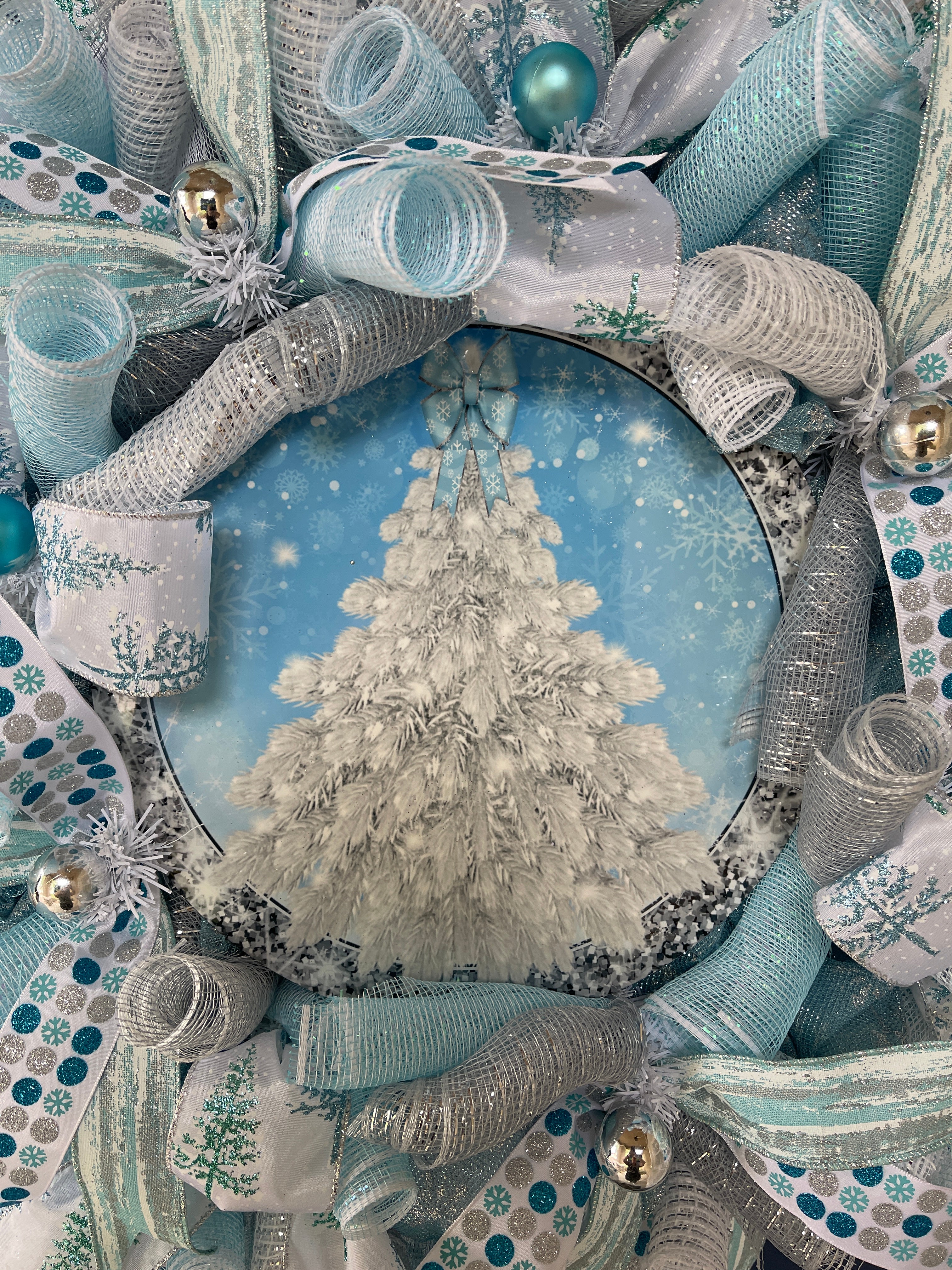 Close Up Detail of Blue Round Metal Sign with a White Flocked Christmas Tree with a Blue Bow