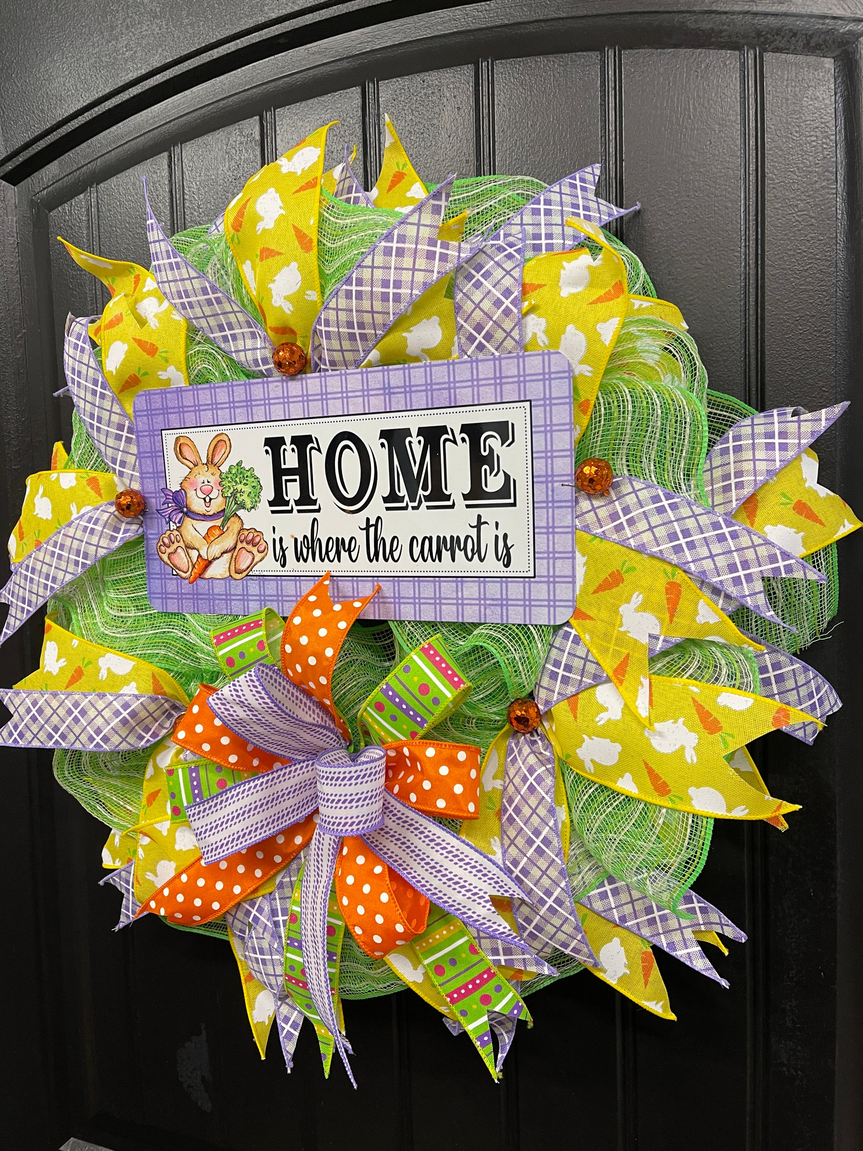 Right Side View of Home is Where the Carrot Is Easter Bunny Wreath with Yellow, Purple, Green, Orange and White Ribbons and Bow on a Black Door