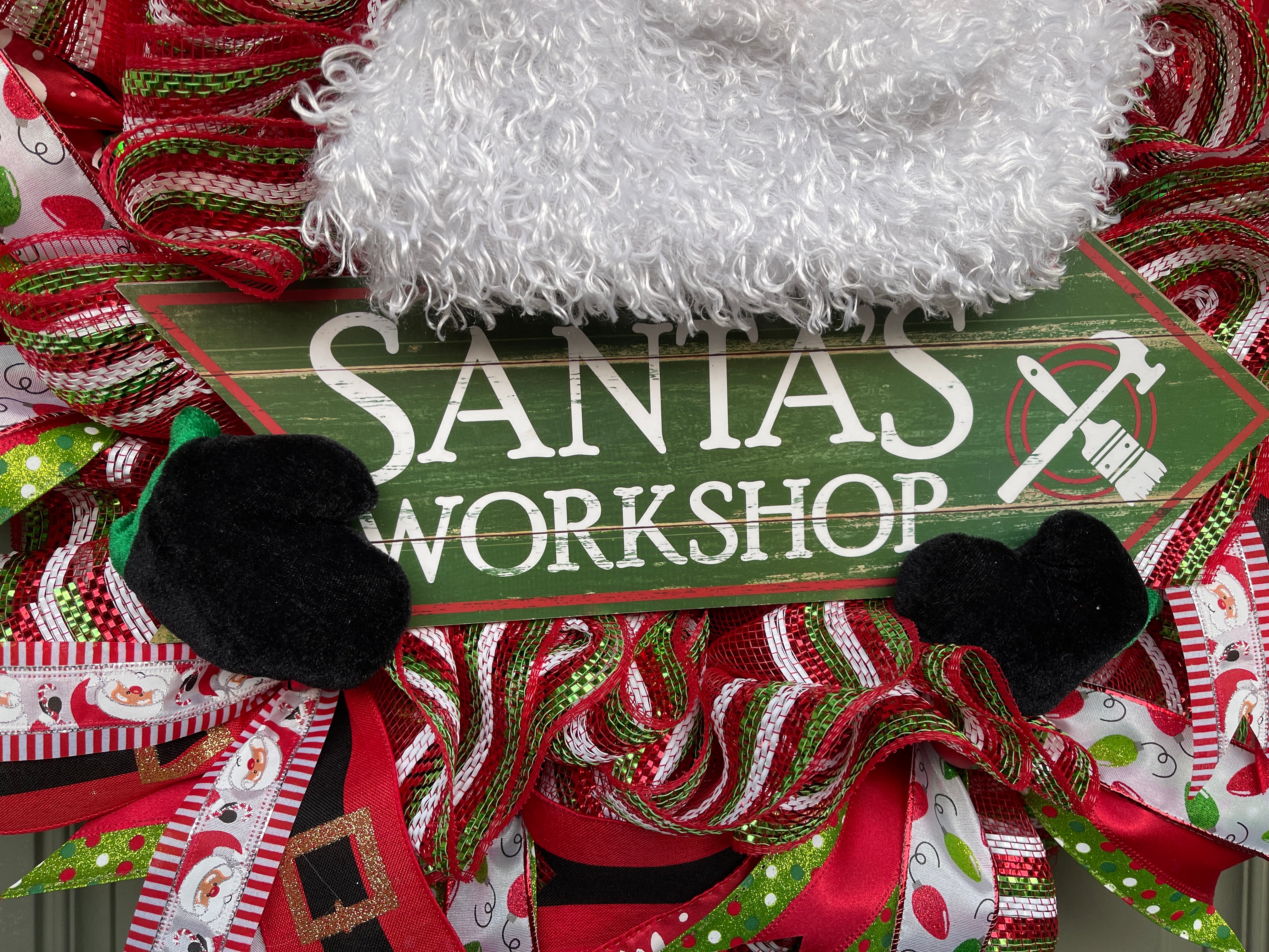 Close Up of Green Wood Santa's Workshop sign in white with a hammer and paint brush logo