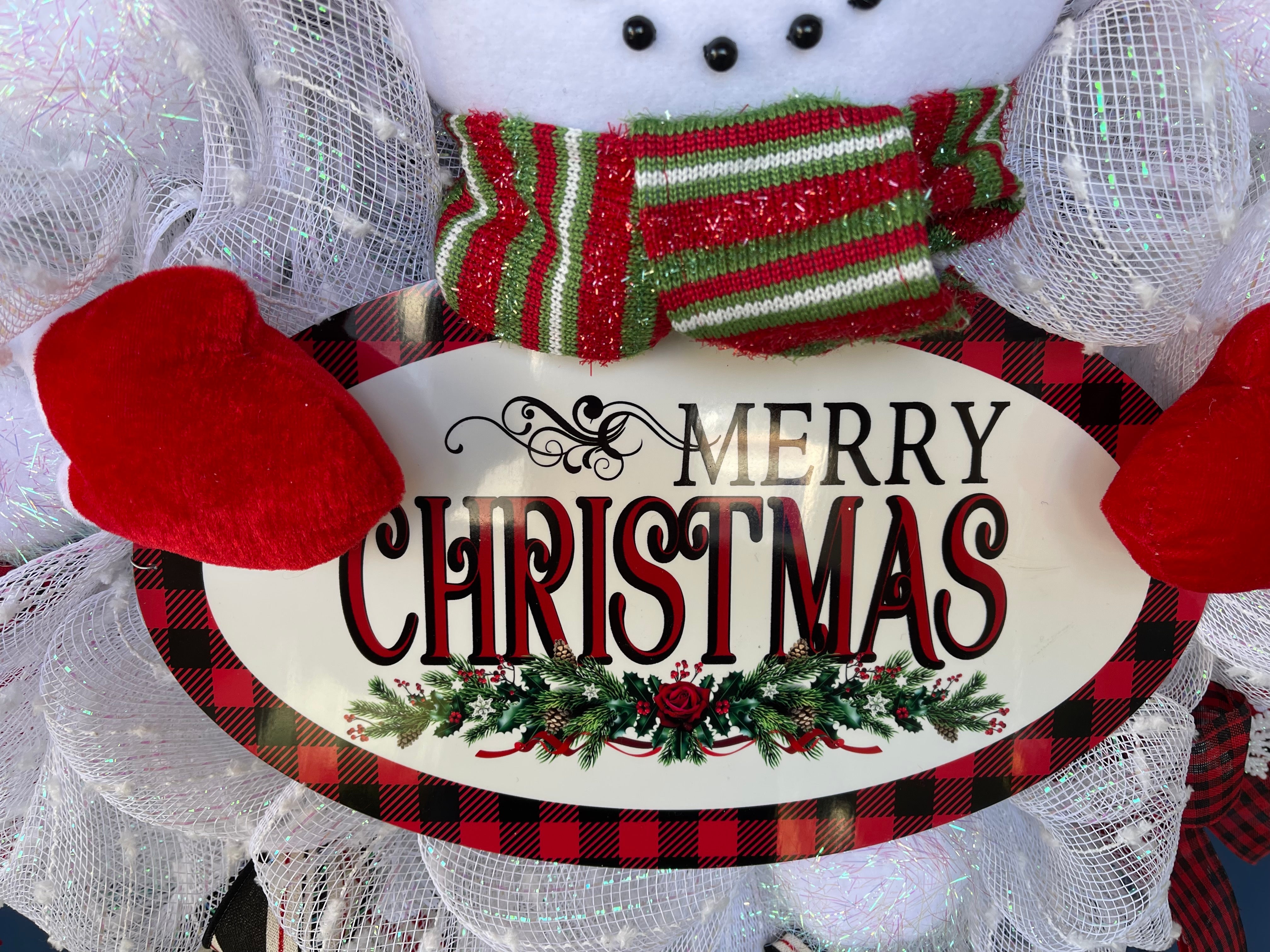 Close Up Detail of Black and Red Buffalo Plaid Bordered Oval  Sign with the words Merry Christmas with garland that the Snowman holds