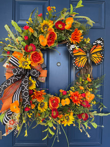 Orange and Yellow Monarch Butterfly Sunflower and Ranunculus Floral Grapevine Wreath with a Bow on a blue door. 