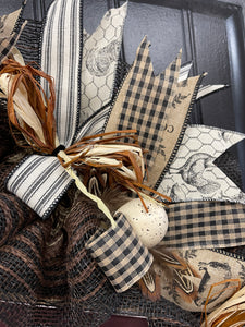 Close Up of Black, White, Tan and Brown Ribbons with Brown and Beige Raffia along with a cream colored speckled egg, chicken feathers on a wreath