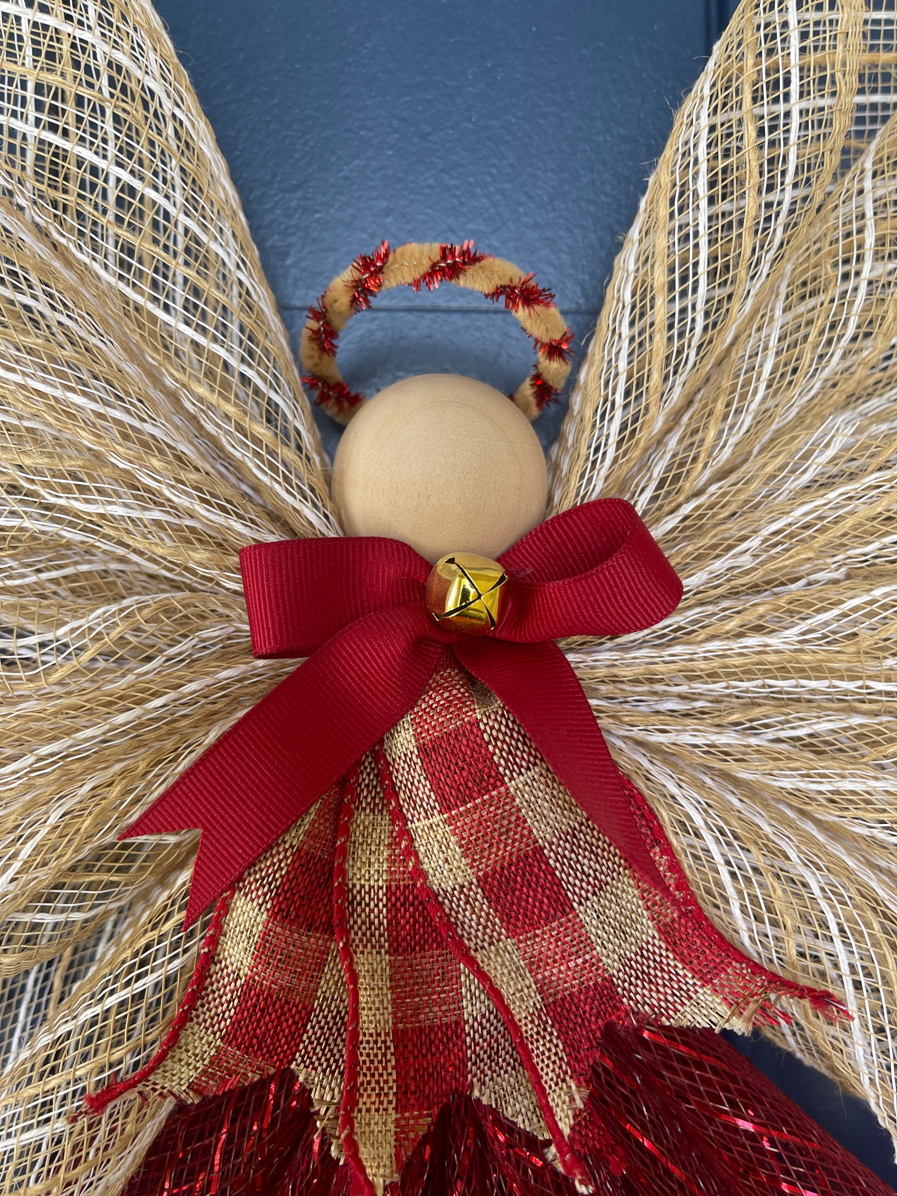 Close Up View of Wooden Head, with a Tan and Red Metallic Halo, Gold Bell on a Red Bow and Red and Tan Plaid Apron 