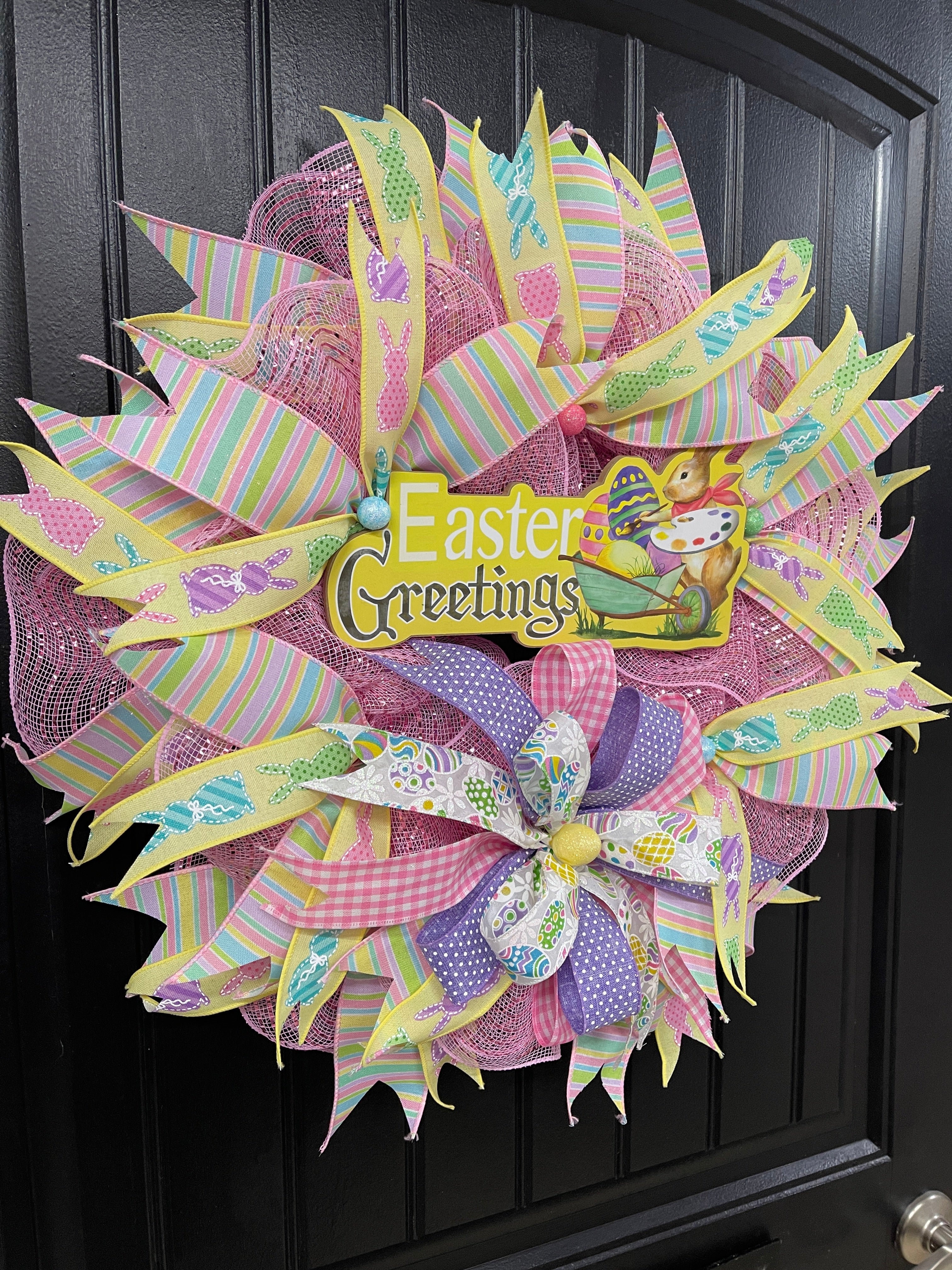 Left Side View of Easter Greetings Bunny Wreath with Pink, Yellow, Blue, Green and Purple Pastel Ribbons and Bows on a Black Door