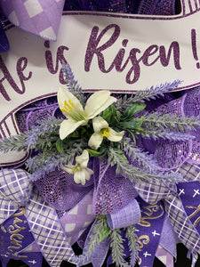Close Up pf He Is Risen White and Purple Banner Sign with White Lilies and Sprigs of Artificial Lavender on a Lavender Deco Mesh Wreath