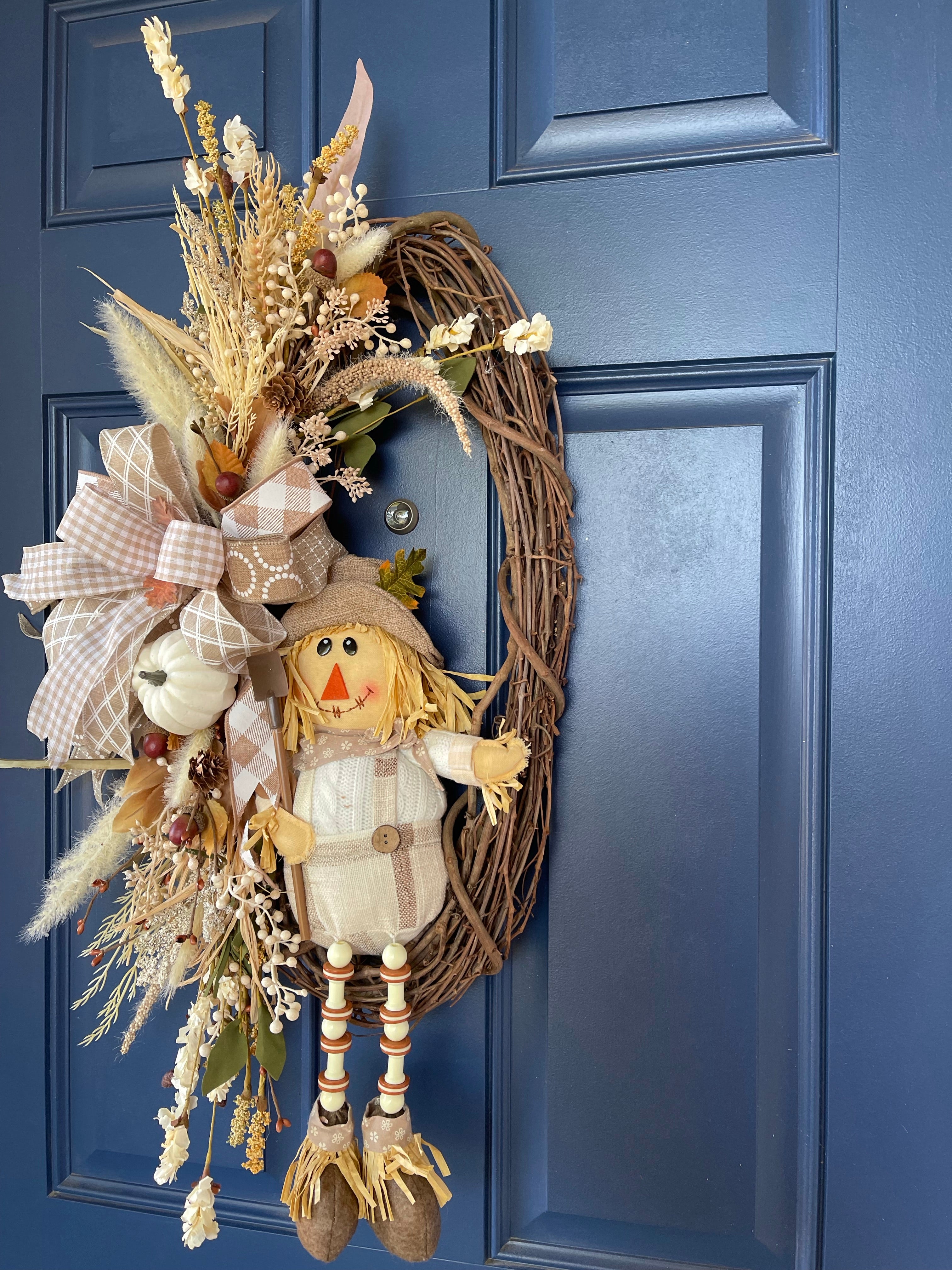 Right Side View of Plush Scarecrow with Shovel on a Grapevine wreath with White, Tan, and Light Brown Florals and Berries on a Blue Door