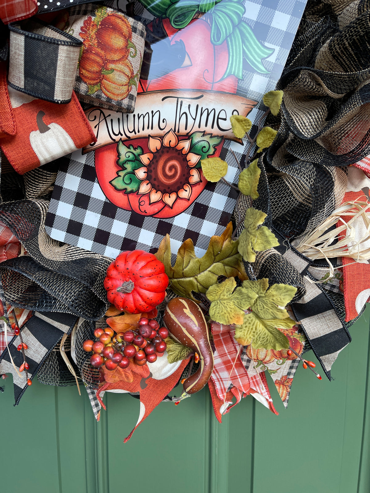 Close Up Details of the Wreath featuring Orange Pumpkins, Brown and Yellow Squash, Fall Berries and Oak Leaves with Raffia and Black, White, Orange and Tan Ribbons