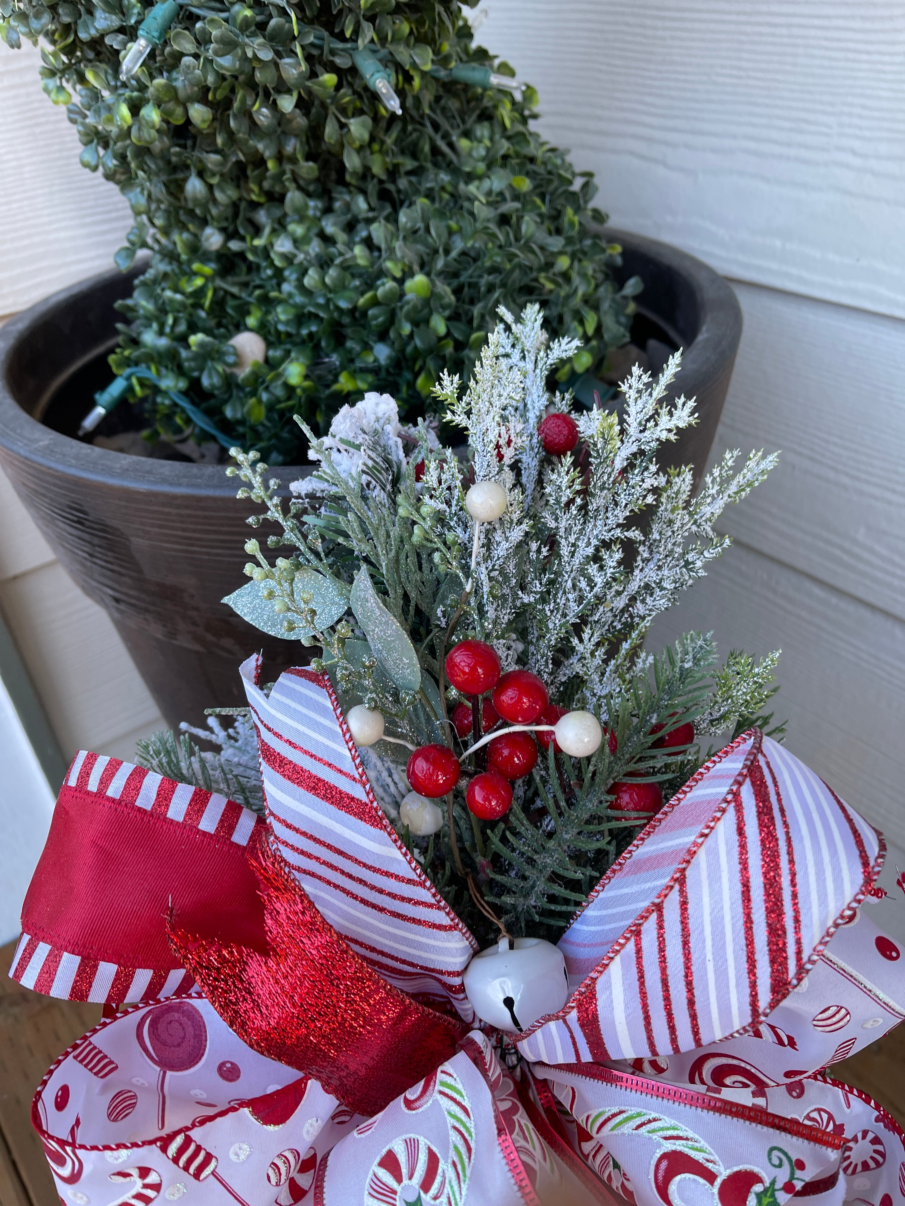Close Up of Red and White Artificial Berries, Frosted Artificial Pine, White Jingle Bells and Red and White Peppermint Striped Ribbons and Bow on a Lantern Swag