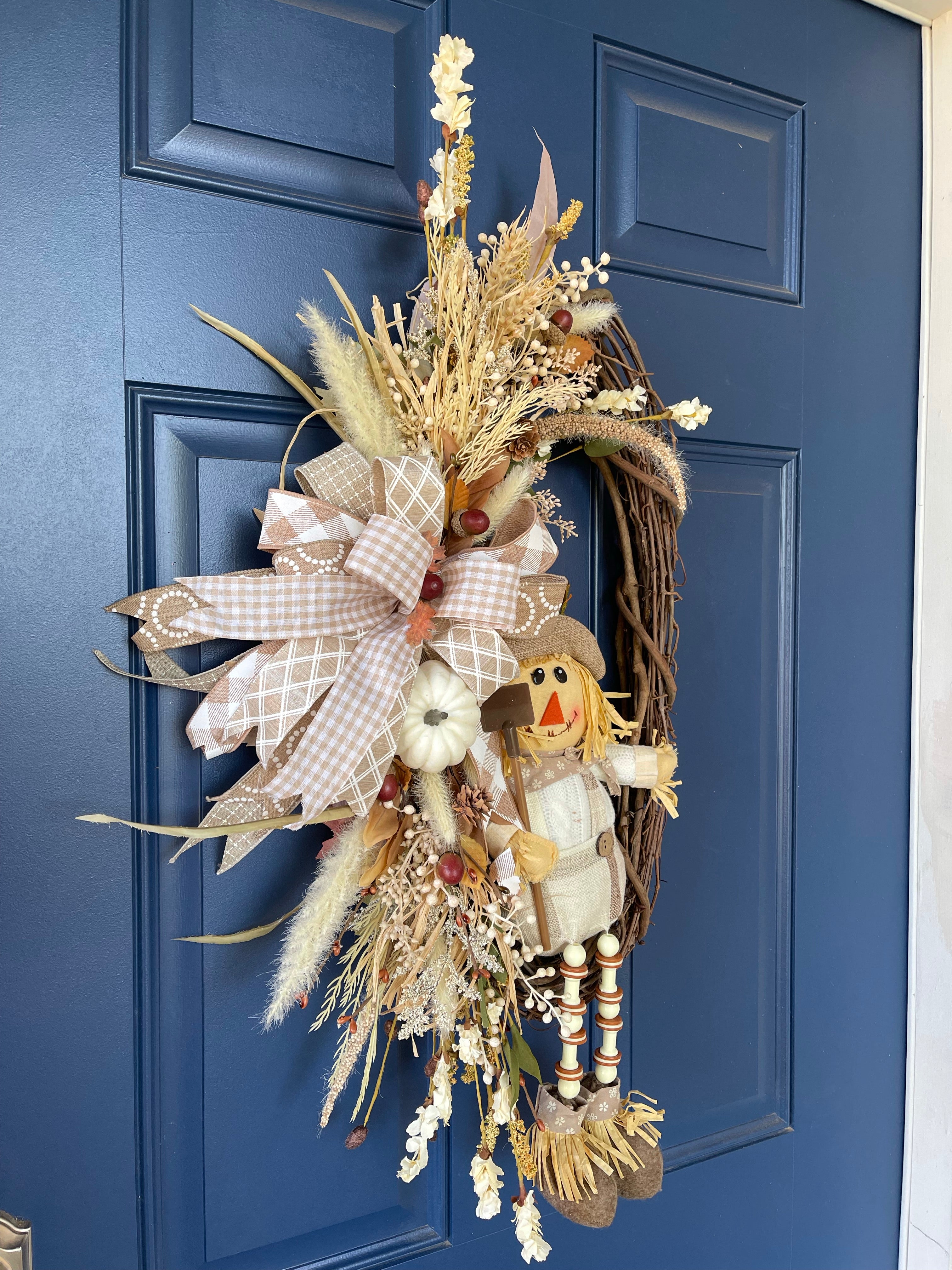 Left Side View of Plush Scarecrow with Shovel on a Grapevine wreath with White, Tan, and Light Brown Florals and Berries on a Blue Door