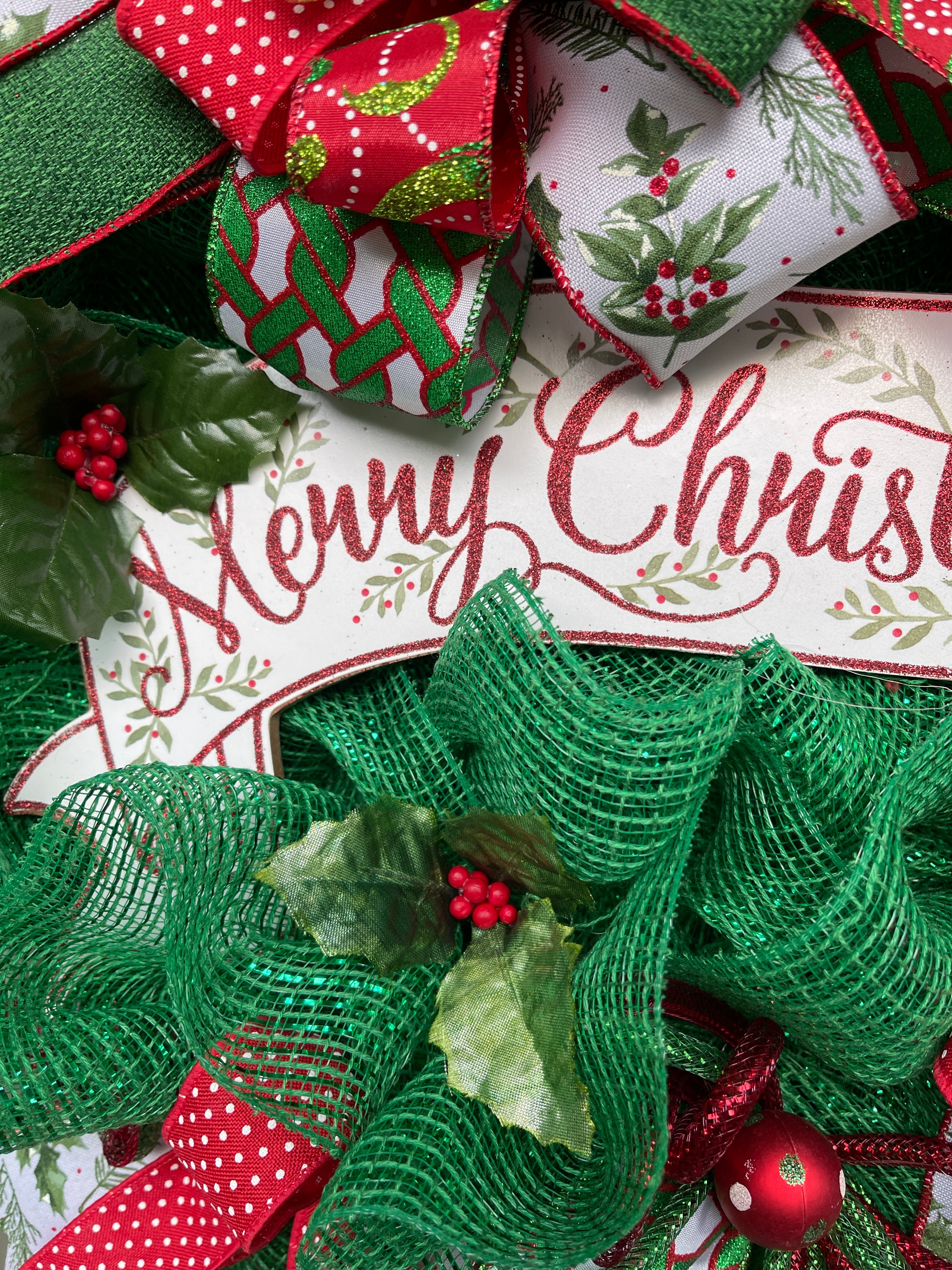 Close Up Detail of Red Words of Merry Christmas on White Banner sign with painted mistletoe branches, sprigs of artificial mistletoe and green fabric mesh