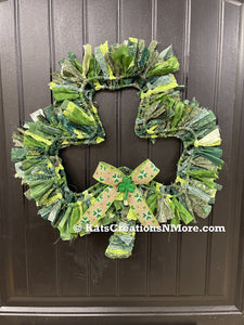 Various Light and Dark Shades of Green Cotton Fabric tied onto a Clover Shaped Frame topped off with a beige and clover ribbon and a glittered green shamrock on a black door. 