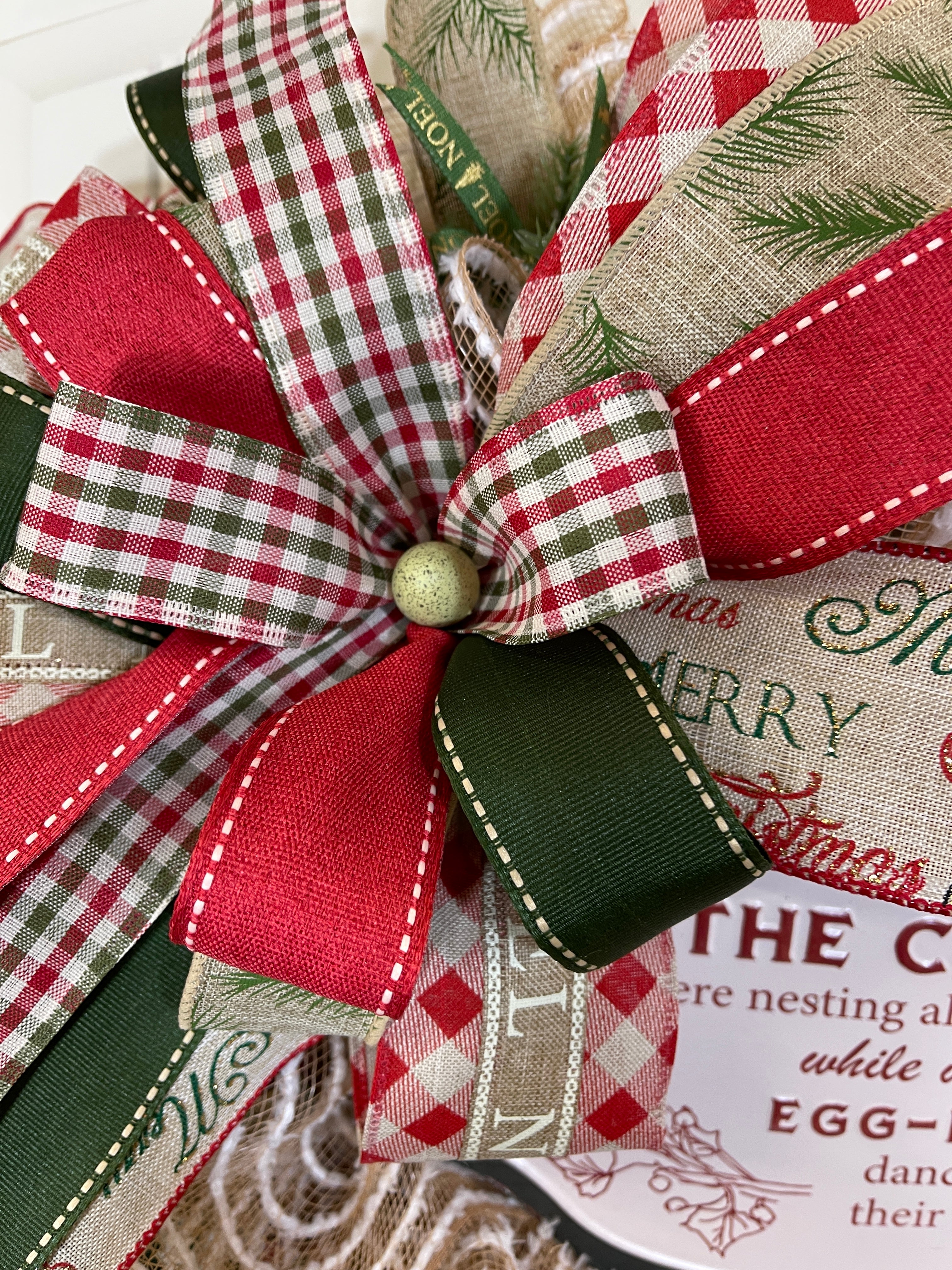 Close Up of Bow with Red, White and Green Gingham Ribbon, Green with Beige Stitching on the Edge Ribbon, Red with Tan Stitching on the Edge of the Ribbon, Merry Christmas Ribbon, Small Green Speckled Egg in the Center of the Bow on a Chicken Christmas Wreath