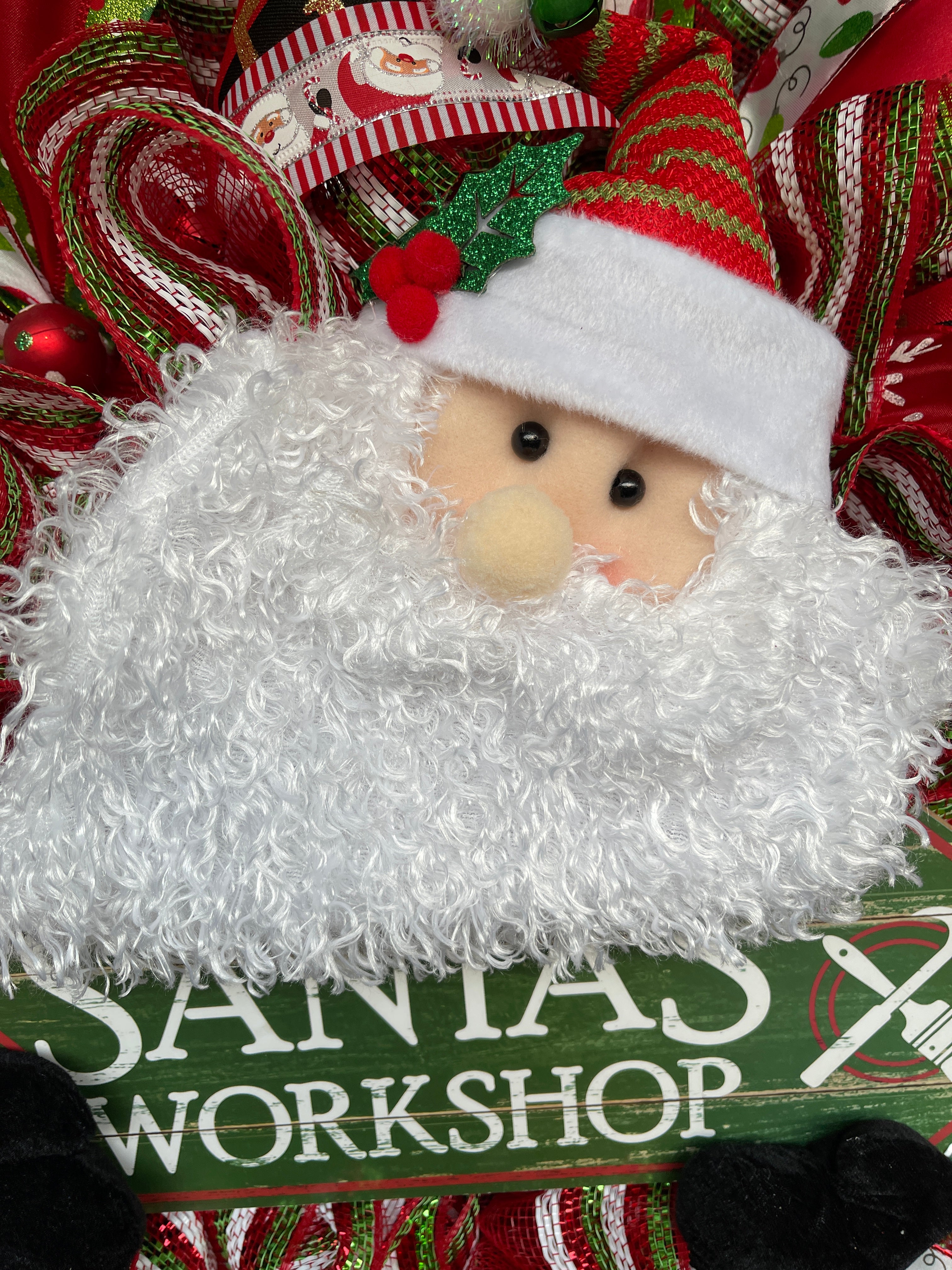 Close Up of Santa Claus Plush Face with White Beard holding a Santa's Workshop Sign