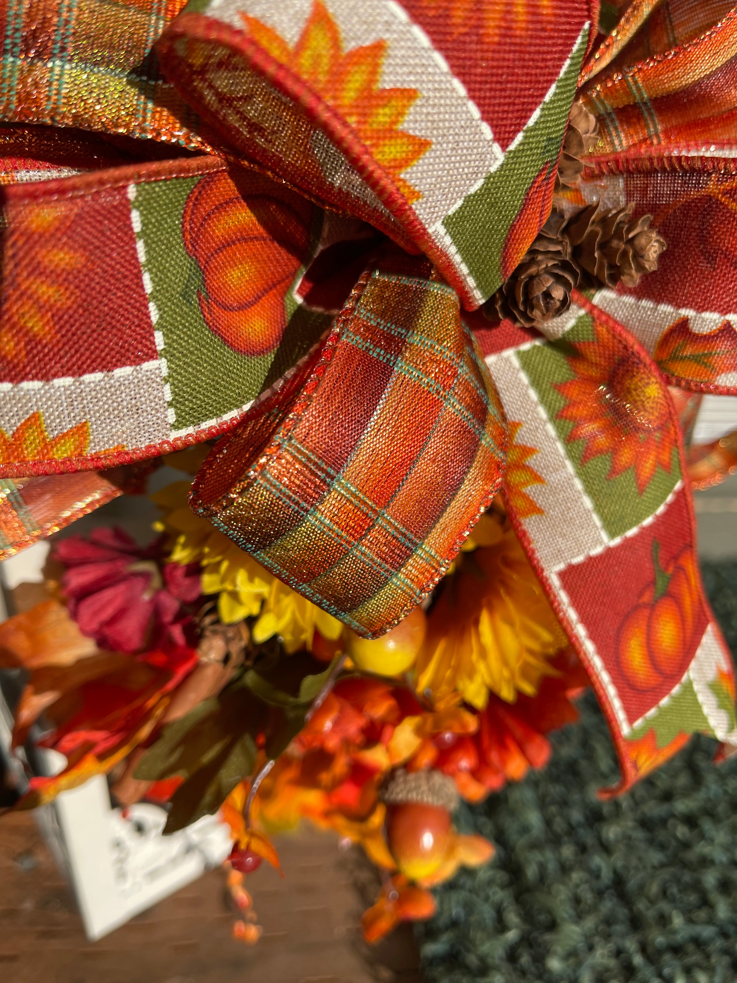 Close Up Detail of Ribbon in Fall Bow with Orange, Red, tan, Green and White, with Pumpkins and Sunflowers on the Print, Pine Cones in the Center of the Bow