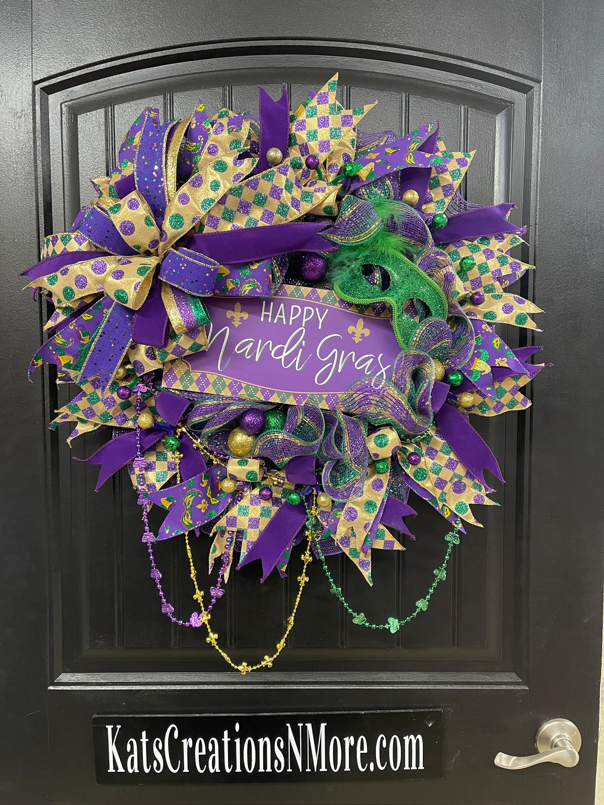 Purple, Green and Gold Mardi Gras Wreath with Beads, Balls, Mask and Bow on a Black Door