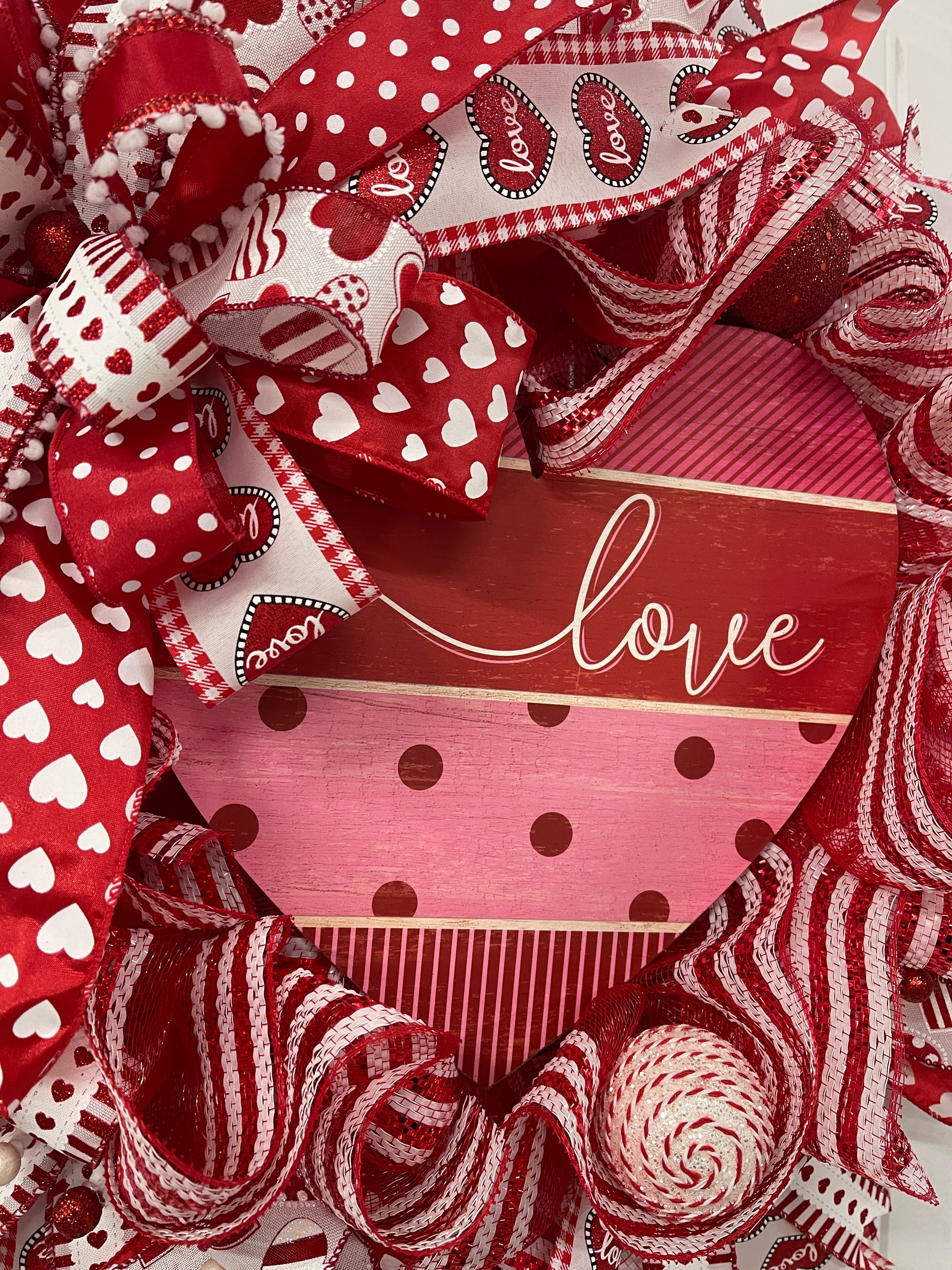 Close Up Detail of a Heart Shaped Red, White and Pink Sign with the Word, "Love" written in script. 