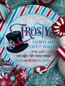 Close Up Detail of Frosty's Snowflake Cafe and Bakery Sign with Black Top Hat, Fresh Snow, Iced Coffee, Hot Cocoa and Cookies, No Hats, No Mittens, No Service with a Plush Snowman next to it.