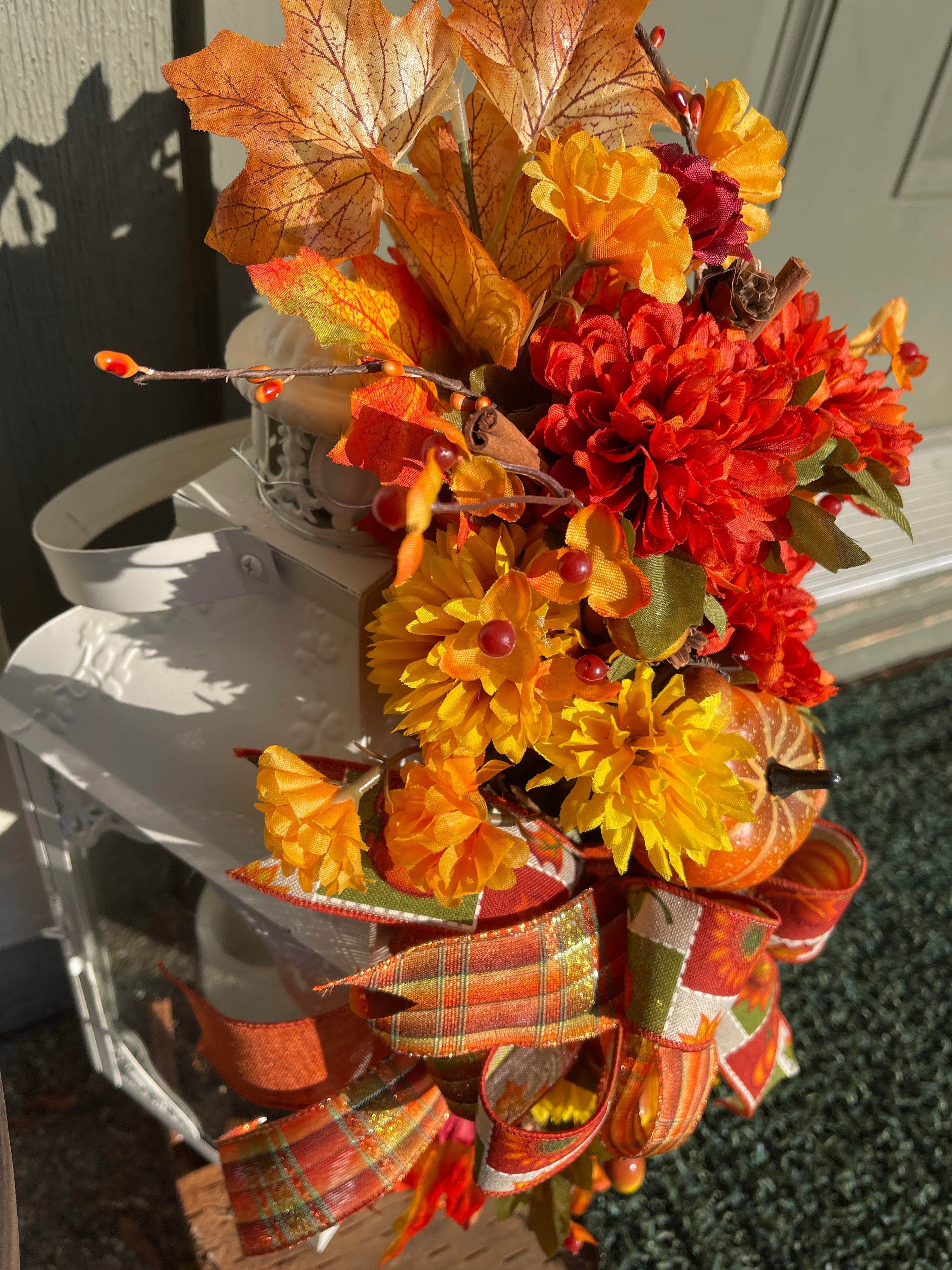 Left Side View of Fall Leaves of Brown, Yellow and Orange, with Orange and Yellow Mums, Pumpkins , Cinnamon Sticks, Red Berries and Pine Cones on a White Lantern on the Porch