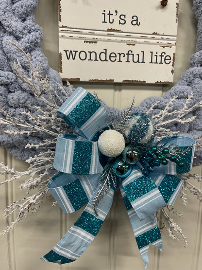 Close Up Detail of Blue and White Bow at the Bottom of the wreath with blue and white balls, silver pine sprigs and white frosted branches. 